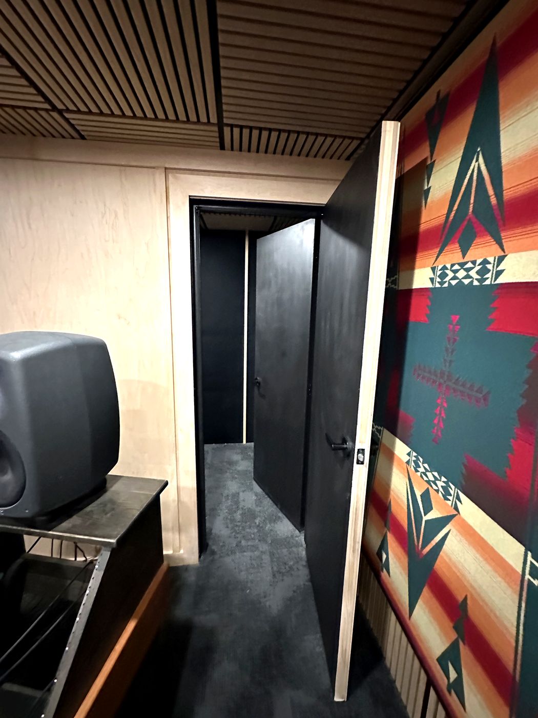 The heavy booth door standing open from the control room, beside a framed acoustic panel.