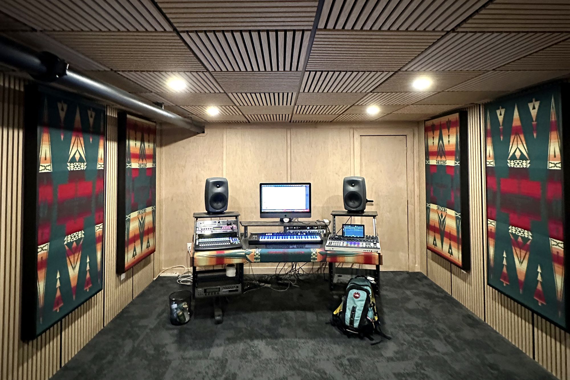 The Fireball Studios control room: slatted wood ceiling, framed blanket-pattern acoustic panels on both walls, and the mix position with a pair of studio monitors at the far end.